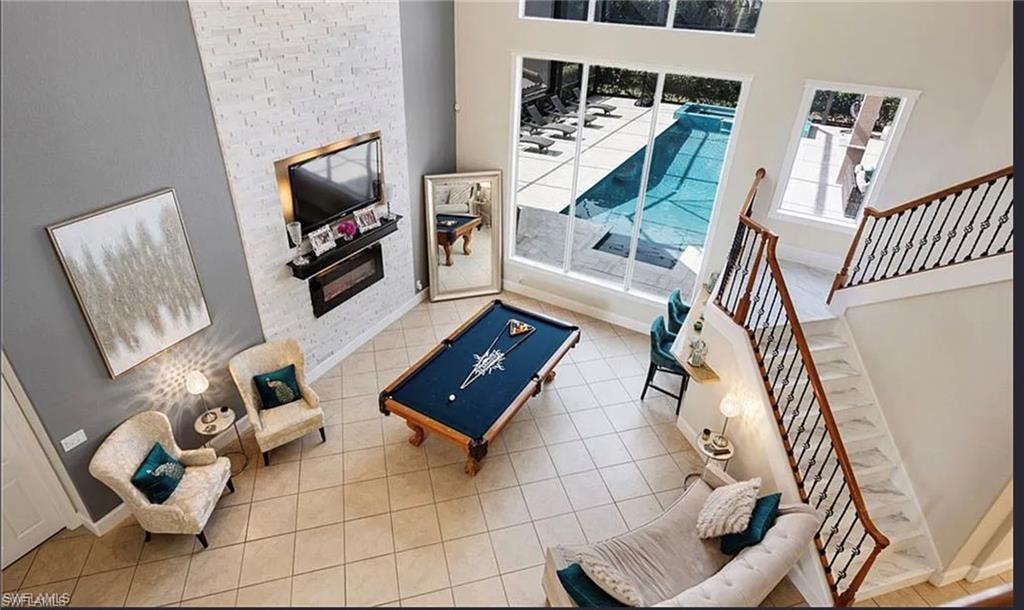 Two-story interior featuring a tiled main floor, a built-in fireplace with a stone-finish accent wall, large windows, and a staircase with an ornamental railing