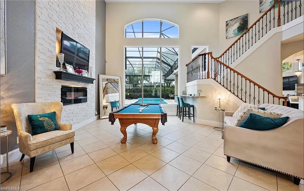 Vaulted ceilings with an arched transom window, a built-in electric fireplace with stone surround, a screened-in pool, and a staircase with decorative wrought iron spindles