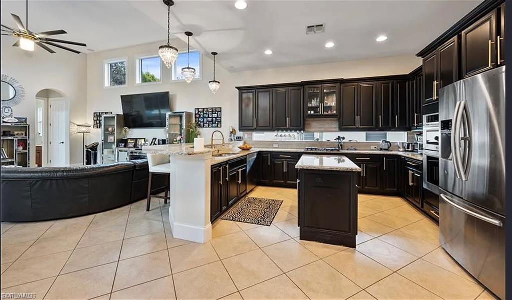 Open-concept kitchen featuring dark wood cabinetry, stainless steel appliances, a center island, and light-toned tile flooring