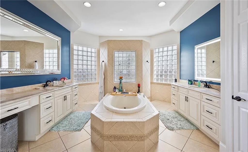 Dual vanities with undermount sinks and extensive counter space, recessed lighting, glass block windows, and a built-in soaking tub