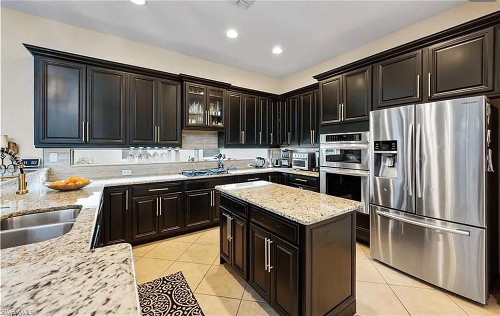 Kitchen featuring dark wood cabinetry, light granite countertops, stainless steel appliances, a center island, and tile flooring