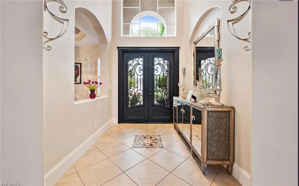 Entryway featuring double doors with decorative ironwork, transom and arched windows, large-format tile flooring with a decorative inset, and arched wall openings