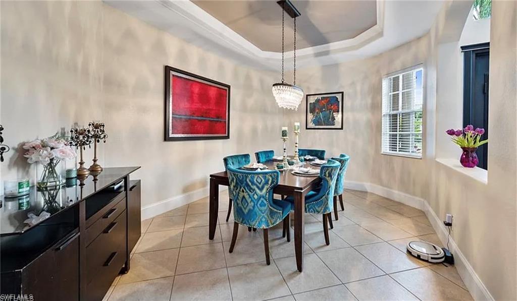 Recessed ceiling with a tiered design, contemporary chandelier, tiled flooring, and a large window with blinds