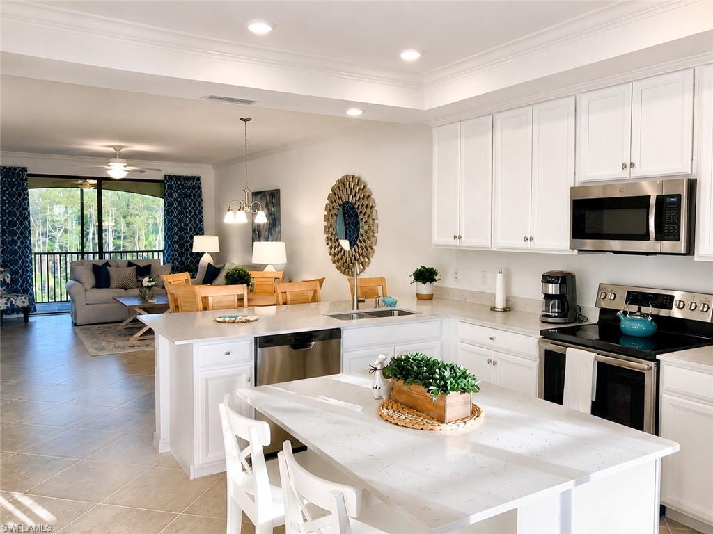 Open-concept kitchen and living area featuring white cabinetry with stainless steel appliances, quartz countertops, a center island with seating, recessed lighting, and a decorative gold-toned circular wall accent
