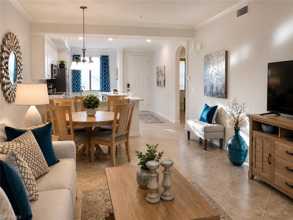 Open-concept living area with tile flooring, a dining area, and a kitchen featuring white cabinetry and a breakfast bar