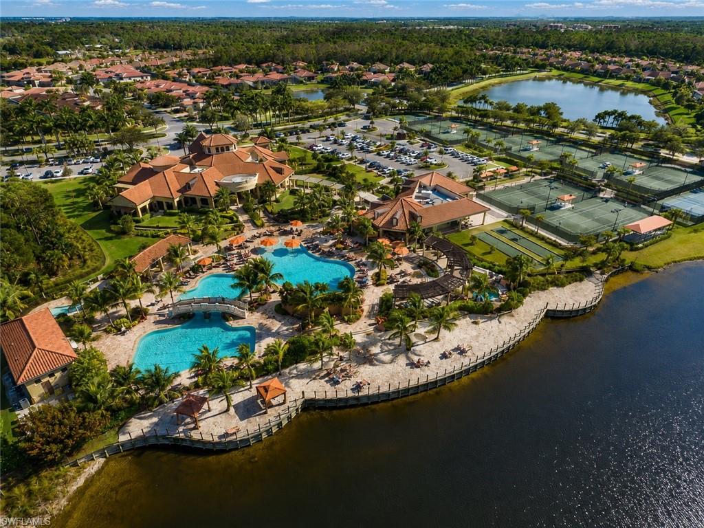 Clubhouse building with a barrel tile roof, multiple swimming pools, extensive hardscaping, multiple tennis courts, and bocce ball courts