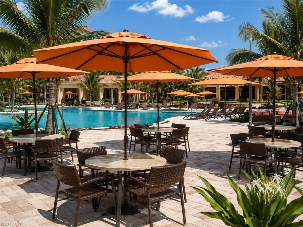 Expansive pool deck with paver surfacing, multiple dining areas with umbrella shading, resort-style swimming pool, and tropical landscaping