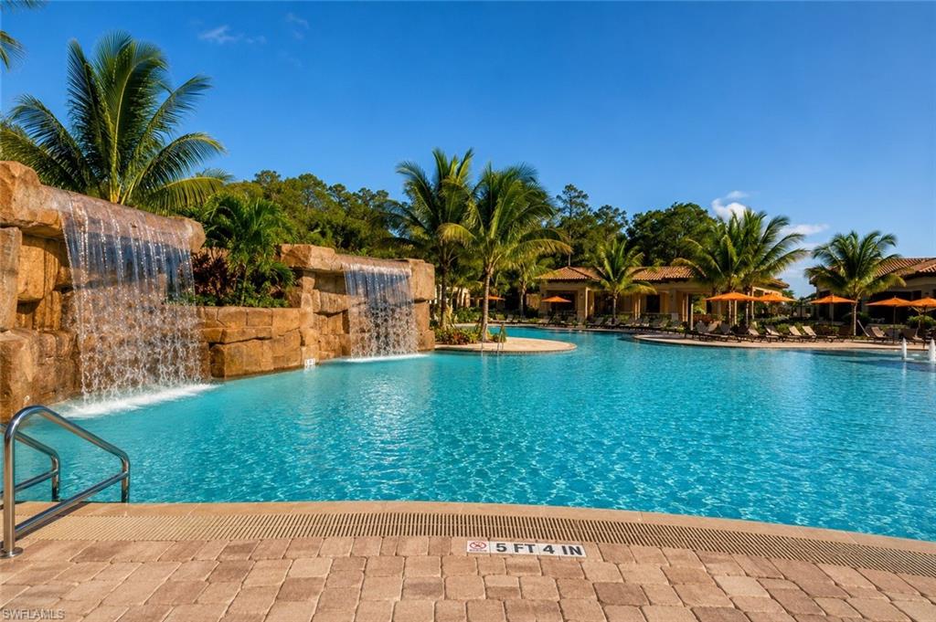 Expansive swimming pool with integrated rock waterfalls, surrounded by mature palm trees and paver decking