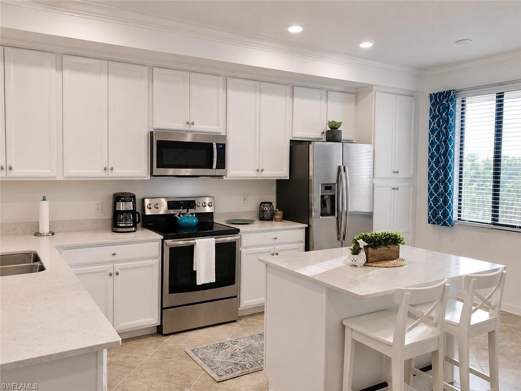 White cabinetry with crown molding, stainless steel appliances, light-toned countertops, a kitchen island, and recessed lighting