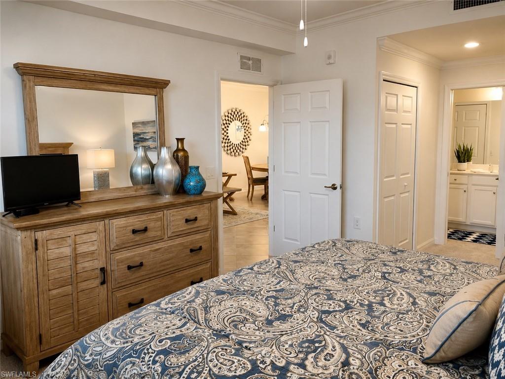Carpeted room with crown molding, a built-in closet, and an open doorway leading to a bathroom featuring a vanity with a countertop and under-sink cabinetry
