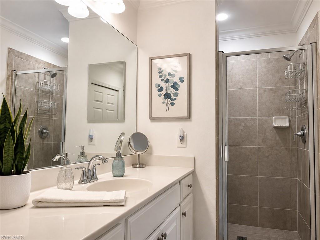 Vanity with integrated sink and chrome faucet, large wall mirror, recessed lighting, and a tiled shower with glass enclosure