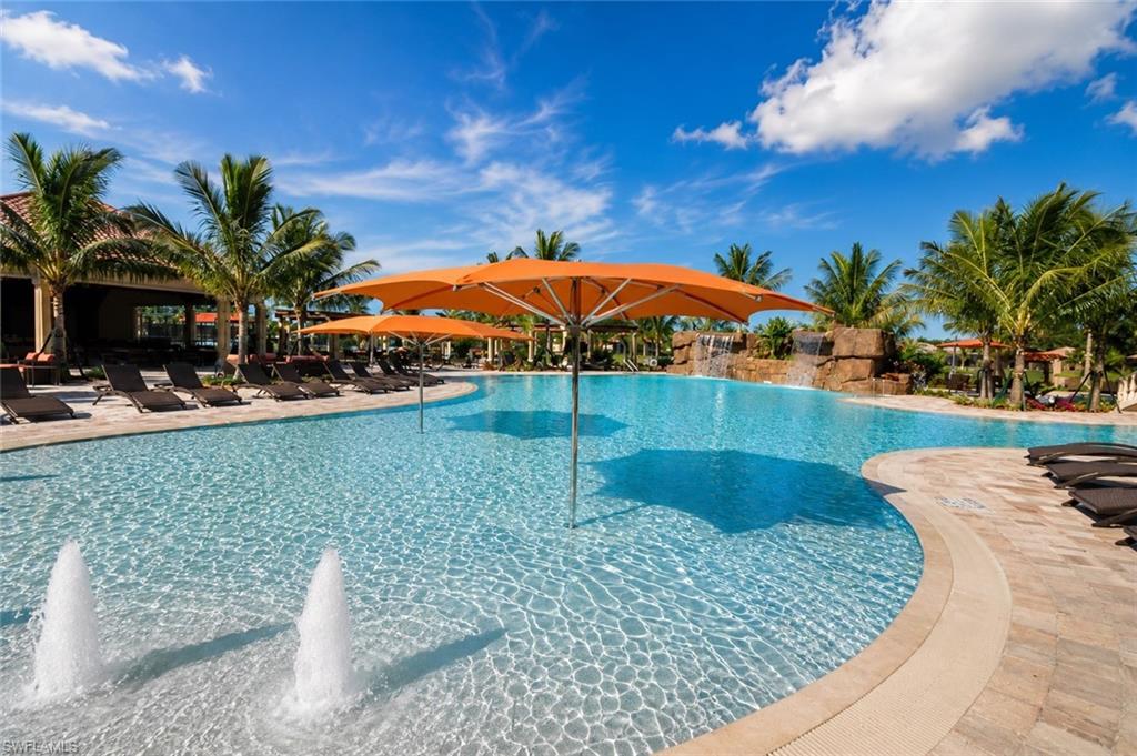 Expansive pool area featuring a large swimming pool with water features, a rock waterfall, and integrated shade umbrellas