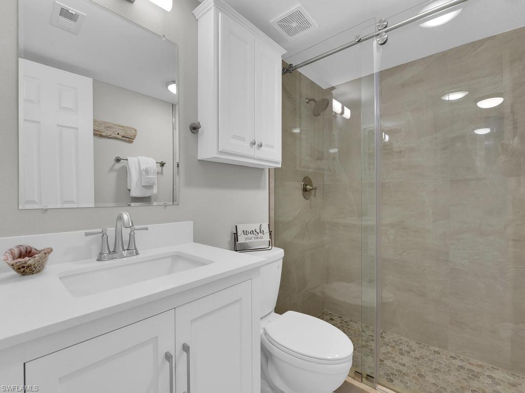 Bathroom featuring a frameless glass shower enclosure with pebble flooring, white shaker vanity with integrated sink, and an overhead medicine cabinet