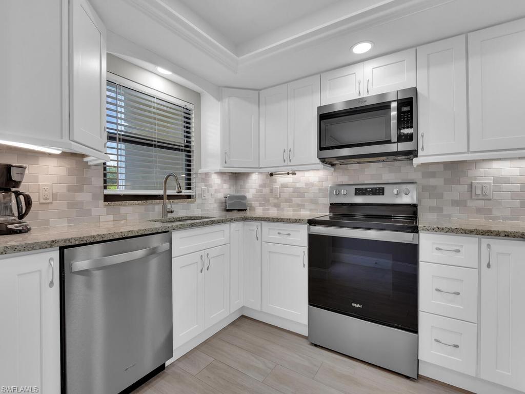 Modern kitchen featuring white shaker cabinetry, stainless steel appliances, a tile backsplash, granite countertops, and wood-finish flooring