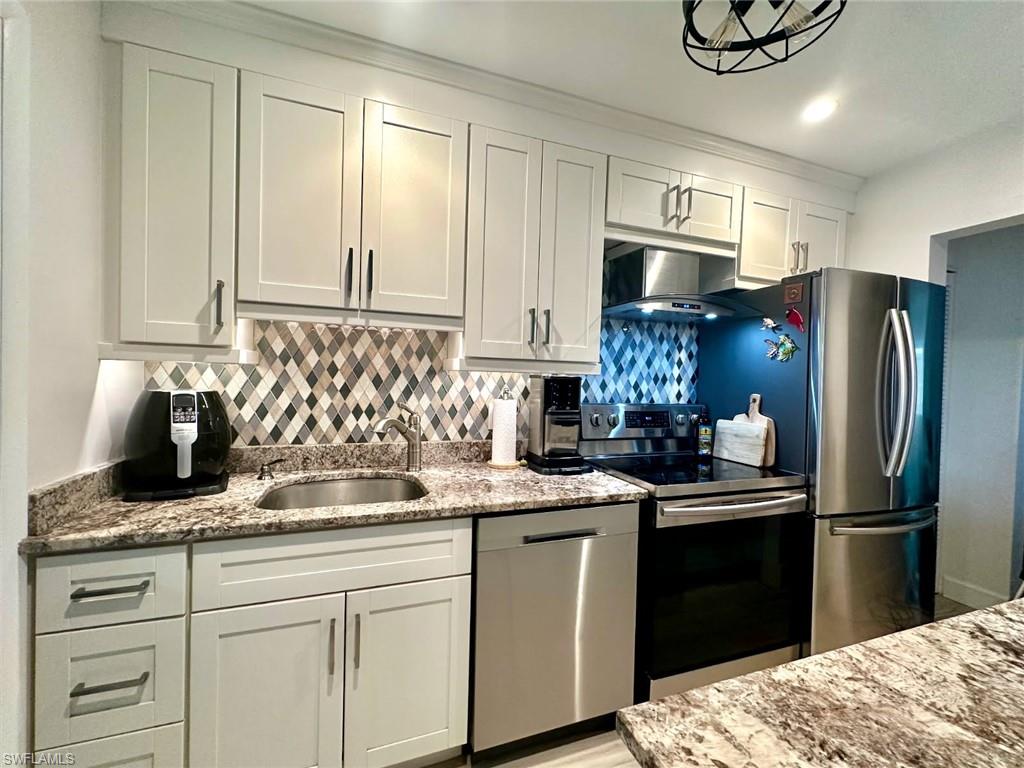 Kitchen featuring stainless steel appliances, light stone counters, white cabinetry, ventilation hood, and backsplash