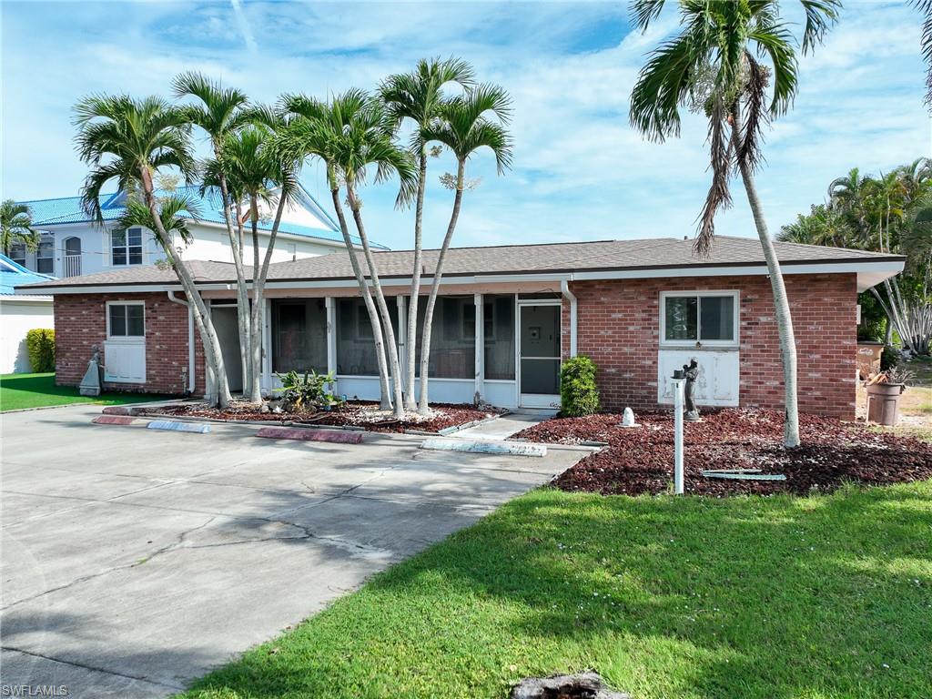 Brick-finish facade with an attached screened-in porch, mature palm trees, and a concrete driveway