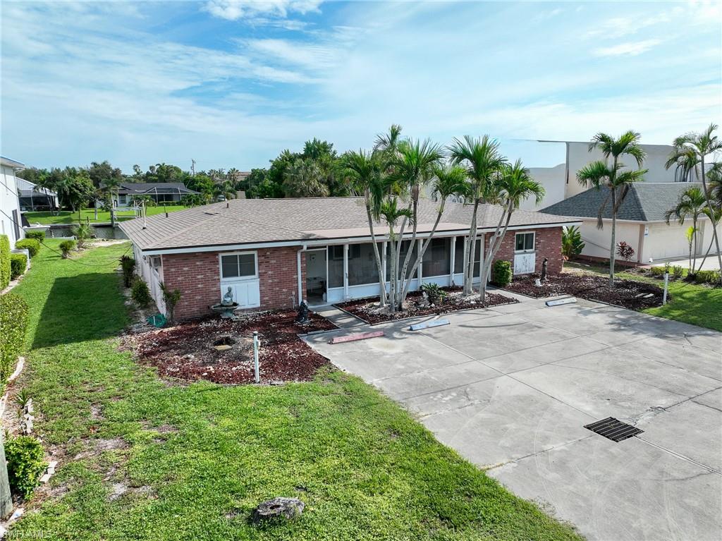 Brick exterior with screened-in entryways, mature palm trees, and a paved parking area