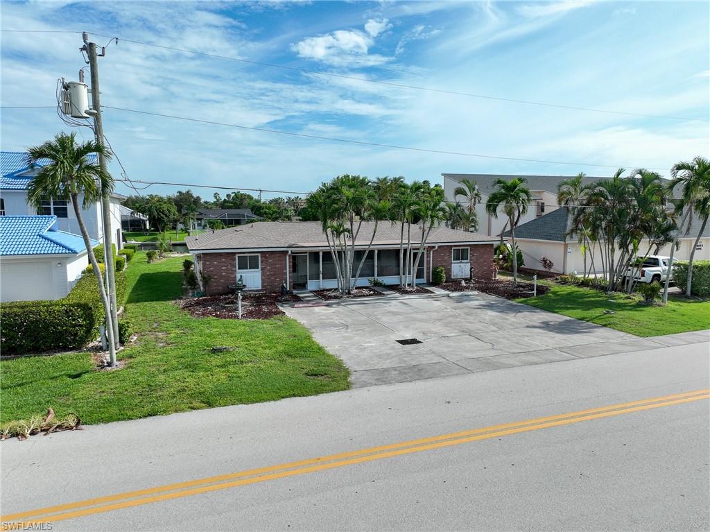 Waterfront property featuring a modern white residence with turquoise metal roof, expansive manicured lawn, mature palm and shade trees, direct water access with dock, and open-concept design visible from the aerial vantage point