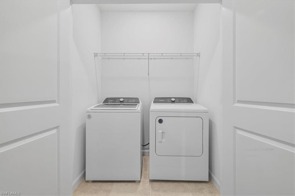 Laundry room with washer and clothes dryer, light tile patterned floors, and baseboards