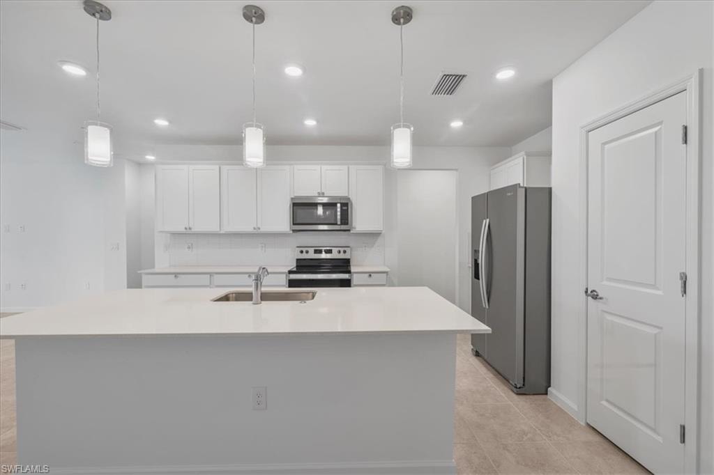 Kitchen featuring stainless steel appliances, a sink, white cabinets, light countertops, and a center island with sink