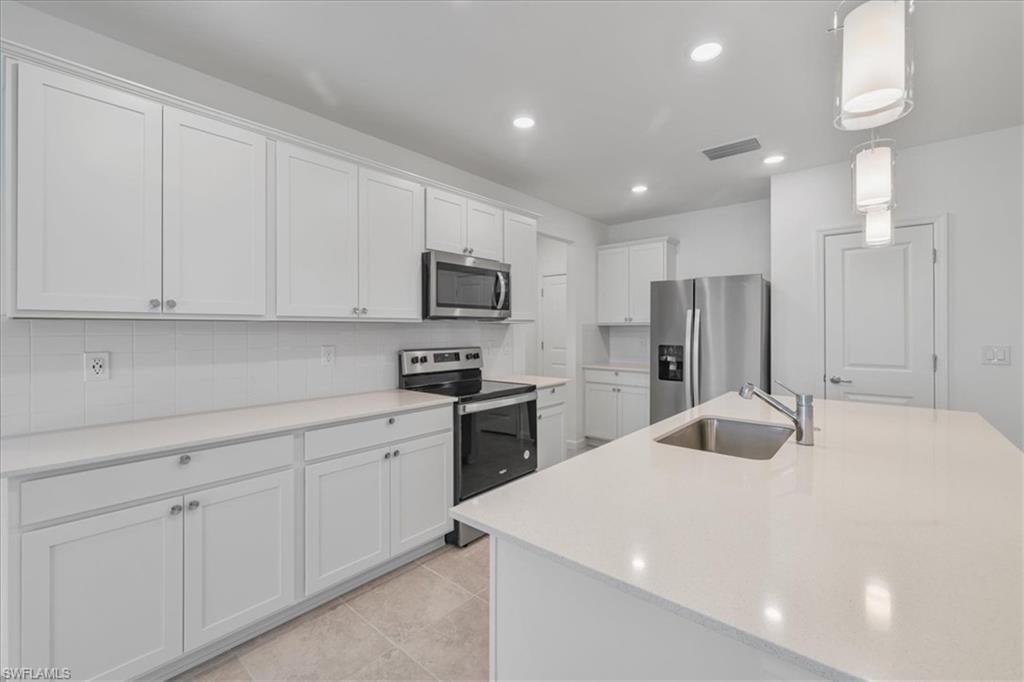 Kitchen with appliances with stainless steel finishes, a sink, backsplash, white cabinetry, and recessed lighting