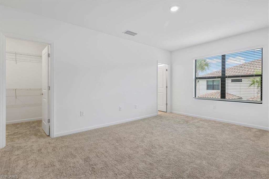 Unfurnished bedroom with light colored carpet, a spacious closet, baseboards, and recessed lighting