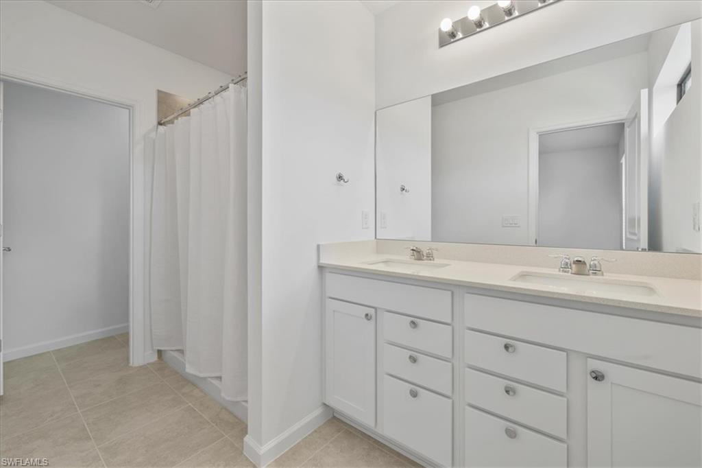 Full bath with double vanity, tile patterned floors, baseboards, and a shower with shower curtain