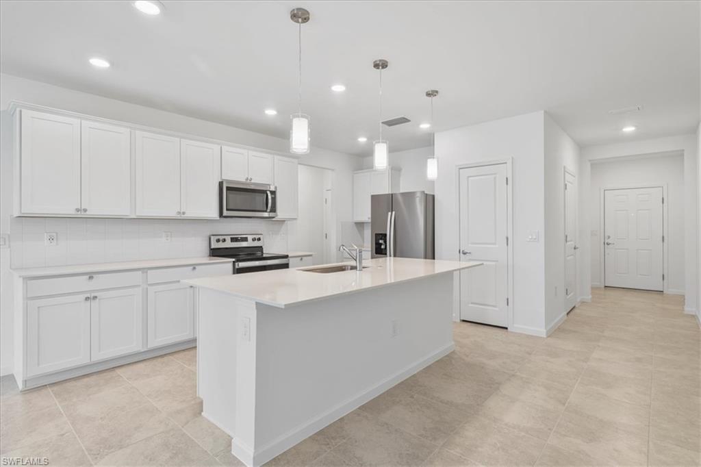 Kitchen with stainless steel appliances, a sink, a center island with sink, white cabinets, and recessed lighting