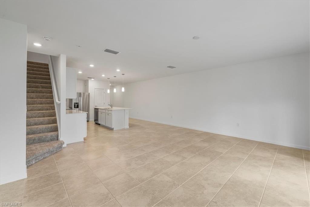 Unfurnished living room featuring stairs, light tile patterned floors, recessed lighting, a sink, and baseboards