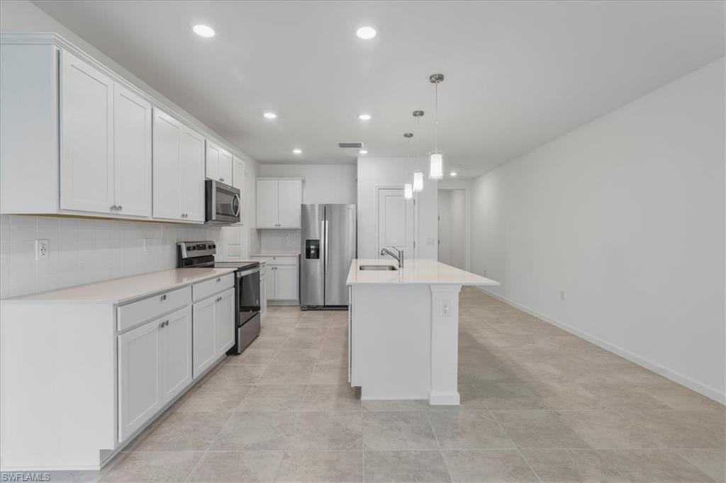 Kitchen featuring appliances with stainless steel finishes, recessed lighting, tasteful backsplash, an island with sink, and white cabinetry