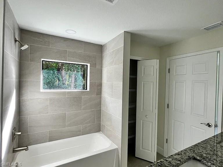 Modern primary bathroom featuring a frameless glass-enclosed shower with linear tile surround, soaking tub, brushed nickel fixtures, recessed ceiling lighting, and a transom window with natural light