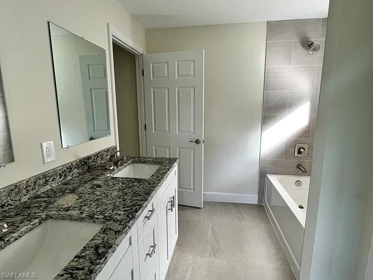 Spa-inspired primary bathroom featuring a granite-topped double vanity with white cabinetry, a walk-in shower with tile surround and rainfall showerhead, soaking tub, and polished concrete flooring throughout