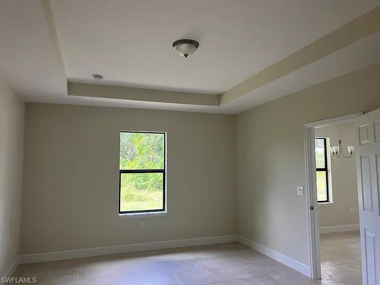 Bright corner bedroom with recessed ceiling detail, large double-hung window with black trim framing natural light, tile flooring, and white six-panel closet doors