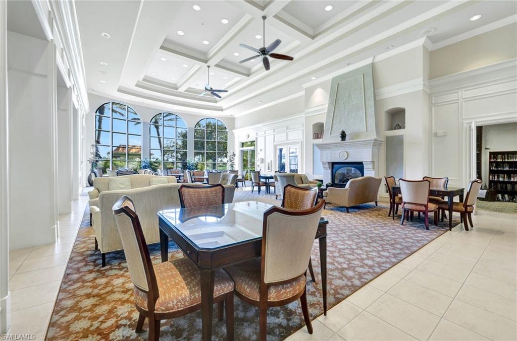 Dining space with a ceiling fan, a towering ceiling, a large fireplace, light tile patterned floors, and coffered ceiling