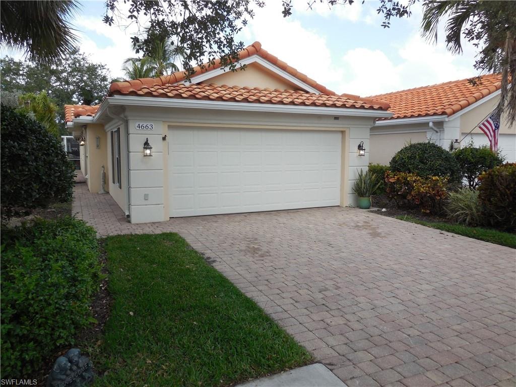View of front facade featuring an attached garage, decorative driveway, stucco siding, and a tile roof