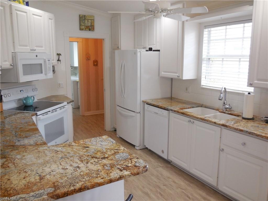Kitchen with white cabinets, a sink, light wood-style floors, white appliances, and backsplash