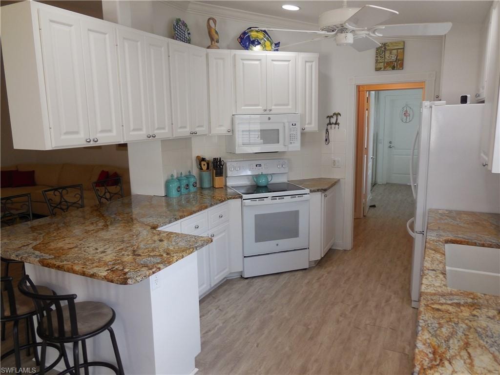 Kitchen with a peninsula, white cabinets, white appliances, and a kitchen breakfast bar