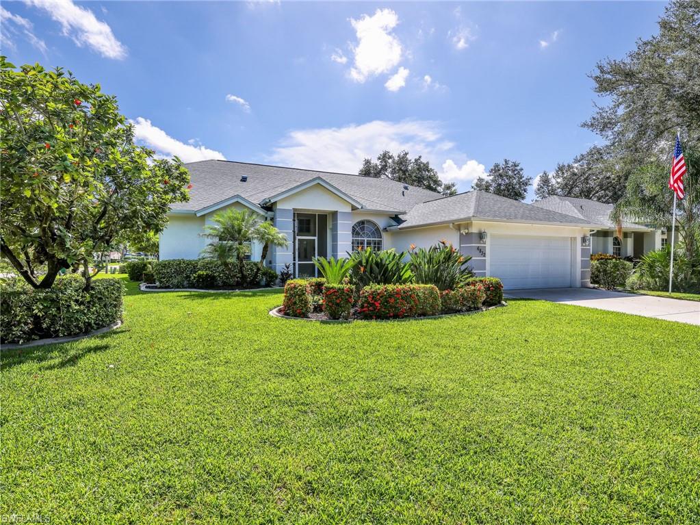Manicured lawn with mature landscaping, attached two-car garage, paved driveway, and covered entry