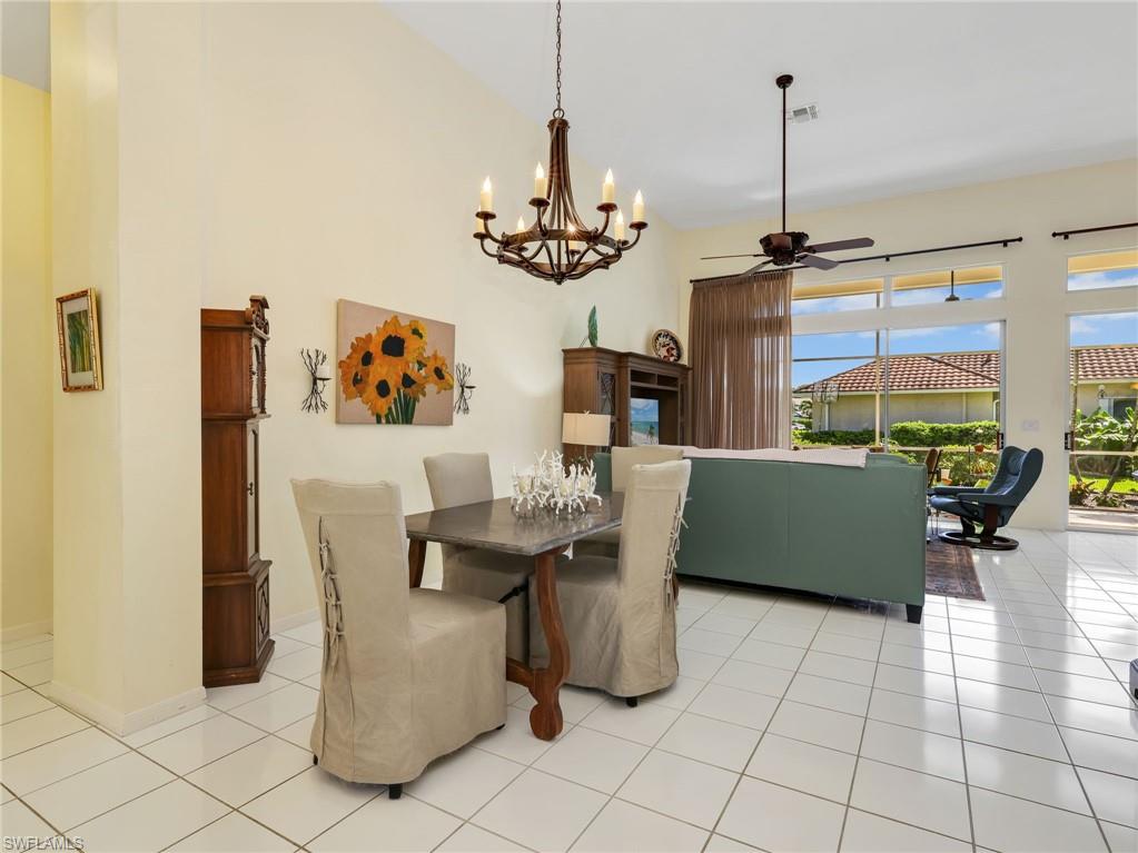 Vaulted ceiling, ceiling fan, tile flooring, large windows, and a chandelier