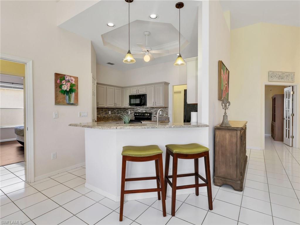 Kitchen featuring light-finish cabinetry, black appliances, a stone-finish backsplash, and an eat-at counter with a stone-finish surface
