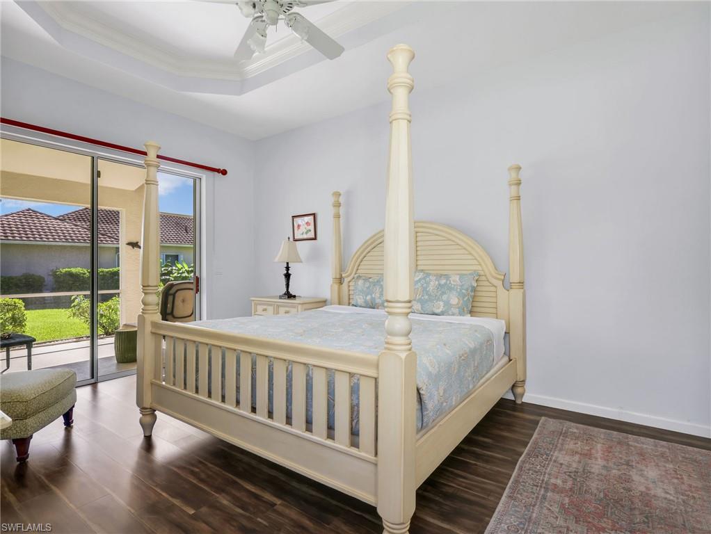 Tray ceiling with a ceiling fan, dark wood-finish flooring, and sliding glass doors to a screened patio