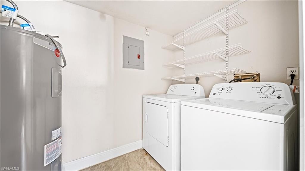 Dedicated laundry room featuring side-by-side washer and dryer units, stainless steel water heater, vinyl plank flooring, wall-mounted shelving for storage, and bright overhead lighting