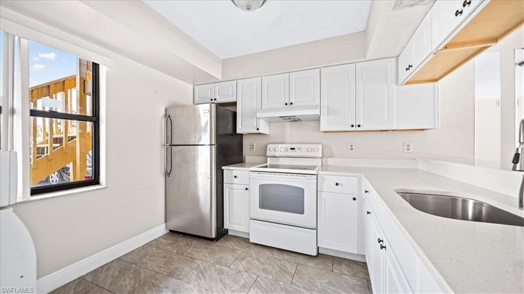 Galley kitchen featuring white cabinetry with hardware accents, stainless steel appliances including a refrigerator and electric range, laminate countertops, and a stainless steel sink
