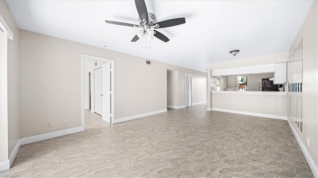 Spacious open living area featuring neutral wall finishes, ceiling fan with integrated lighting, tile flooring throughout, and abundant natural light from multiple windows