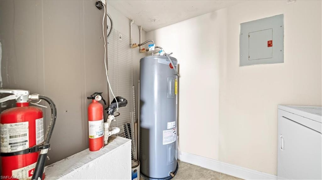 Utility room featuring multiple fire safety systems including dual fire extinguishers, a large water heater with visible connections and controls, and a wall-mounted electrical panel