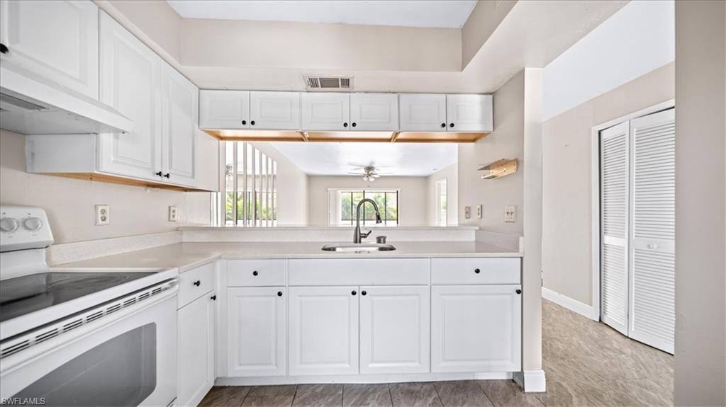 White cabinetry with black hardware, integrated sink, electric range, and wood-finish flooring