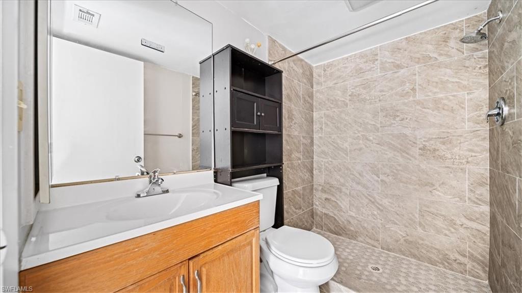 Vanity with integrated sink and chrome faucet, large mirror, built-in shelving, shower with tiled walls, and rain shower head