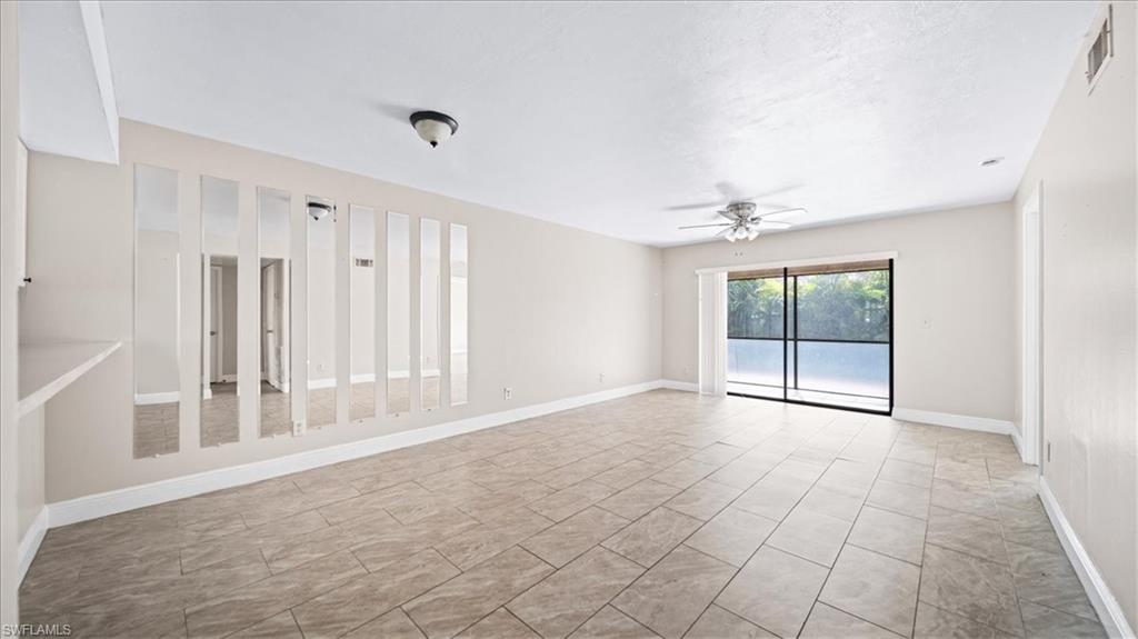 Spacious open-concept living area featuring tile flooring throughout, abundant natural light from sliding glass doors with views to the exterior, and a wall of built-in cabinetry with glass-front doors