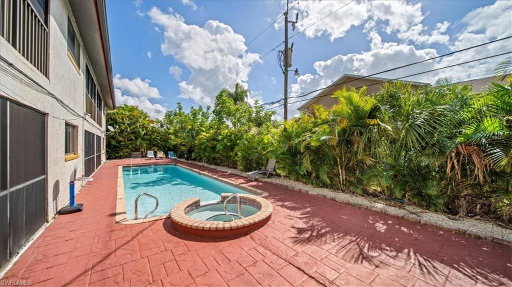 Resort-style backyard oasis featuring a sparkling swimming pool with integrated spa, terracotta-tiled deck, mature tropical landscaping including palm trees, and lush privacy vegetation