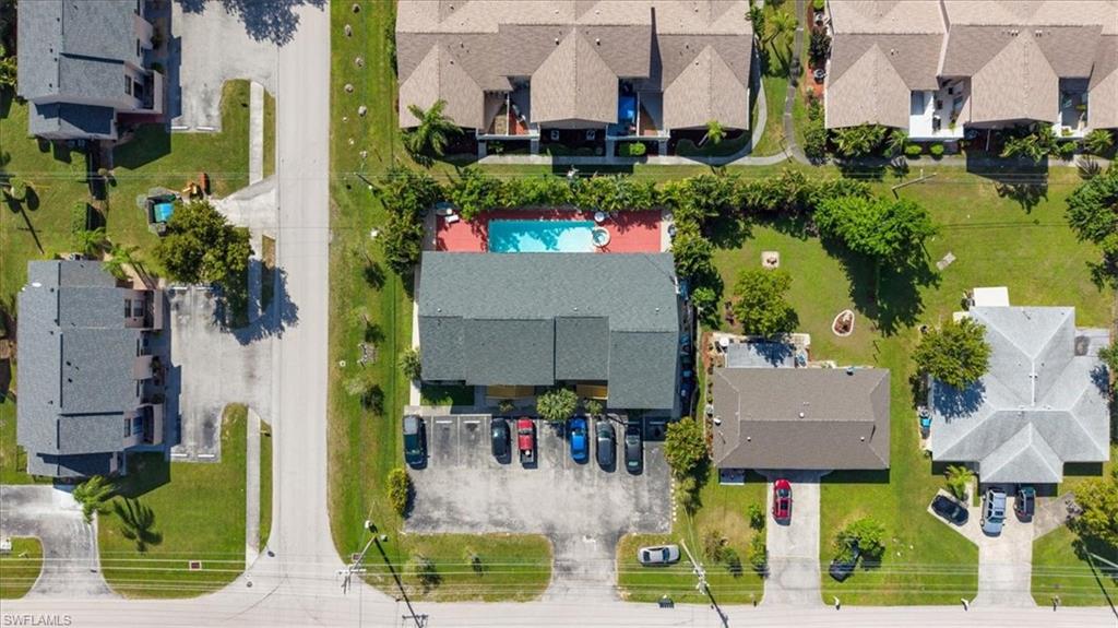 Community pool with surrounding patio, asphalt parking area, and manicured green spaces